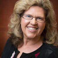 Smiling woman with glasses and curly blonde hair.