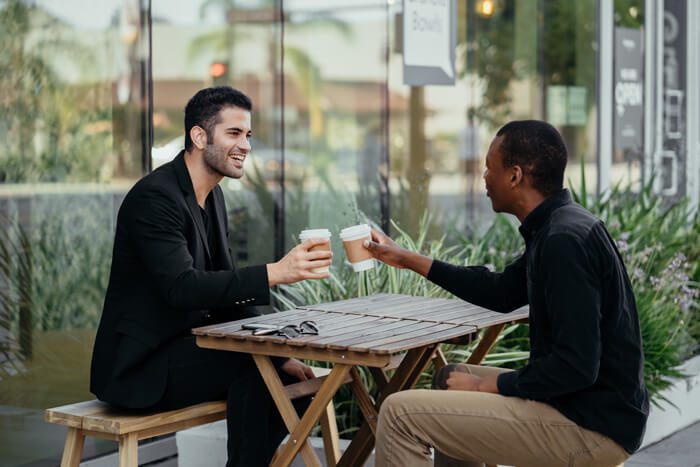 Two men clinking glasses over a meal at a cozy cafe.