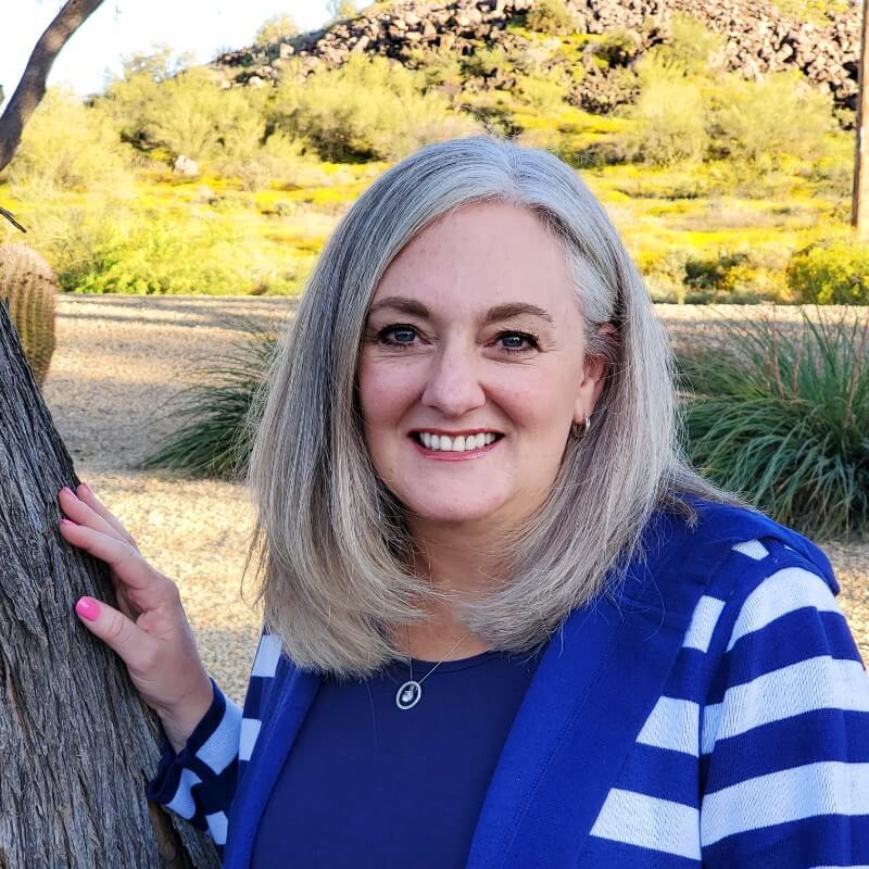 Smiling woman with silver hair wearing a blue and white striped top outdoors.